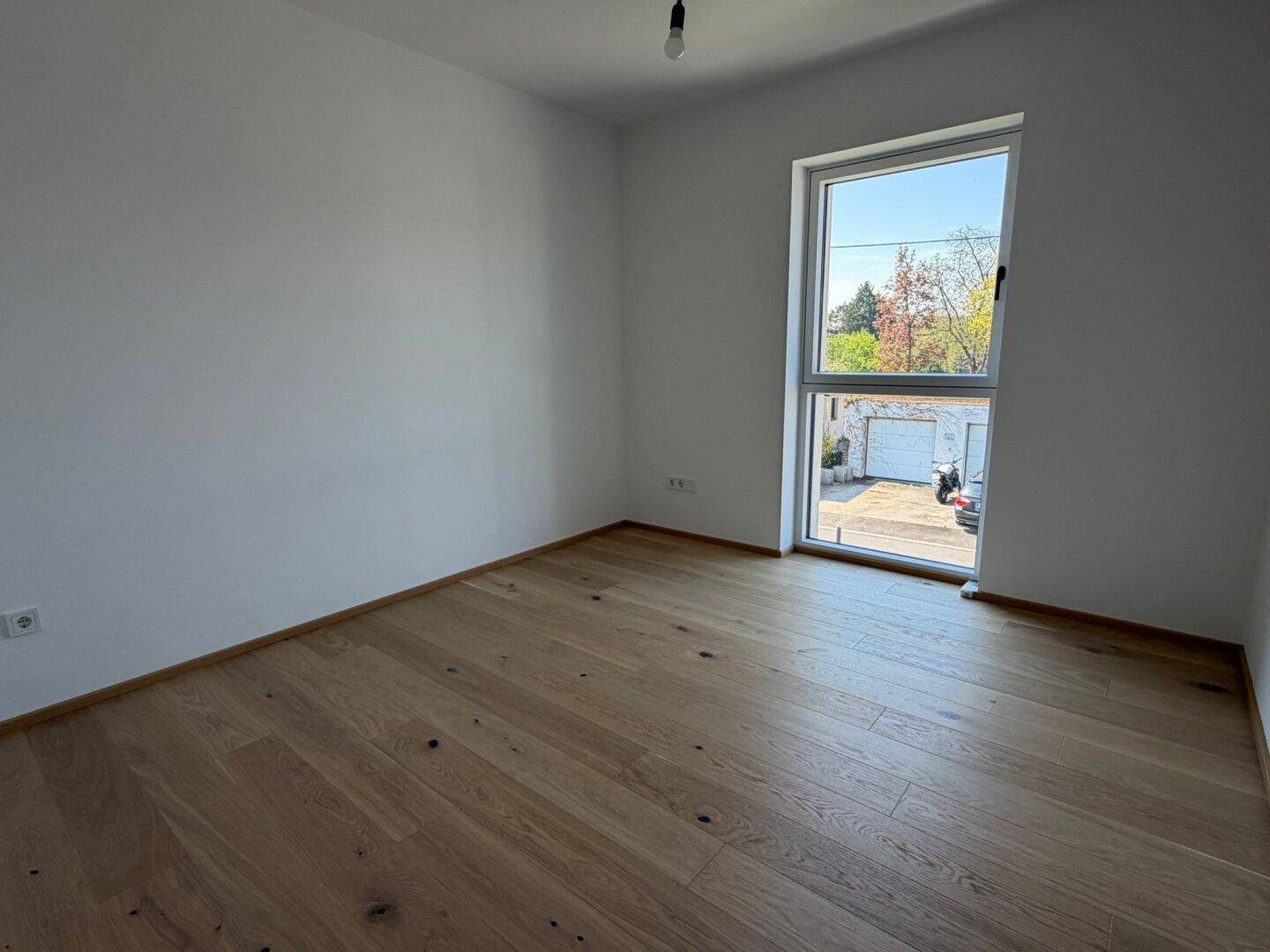 Weiteres Schlafzimmer mit hellem Eichenparkett und großem Fenster, ideal für Gäste oder Kinder.
