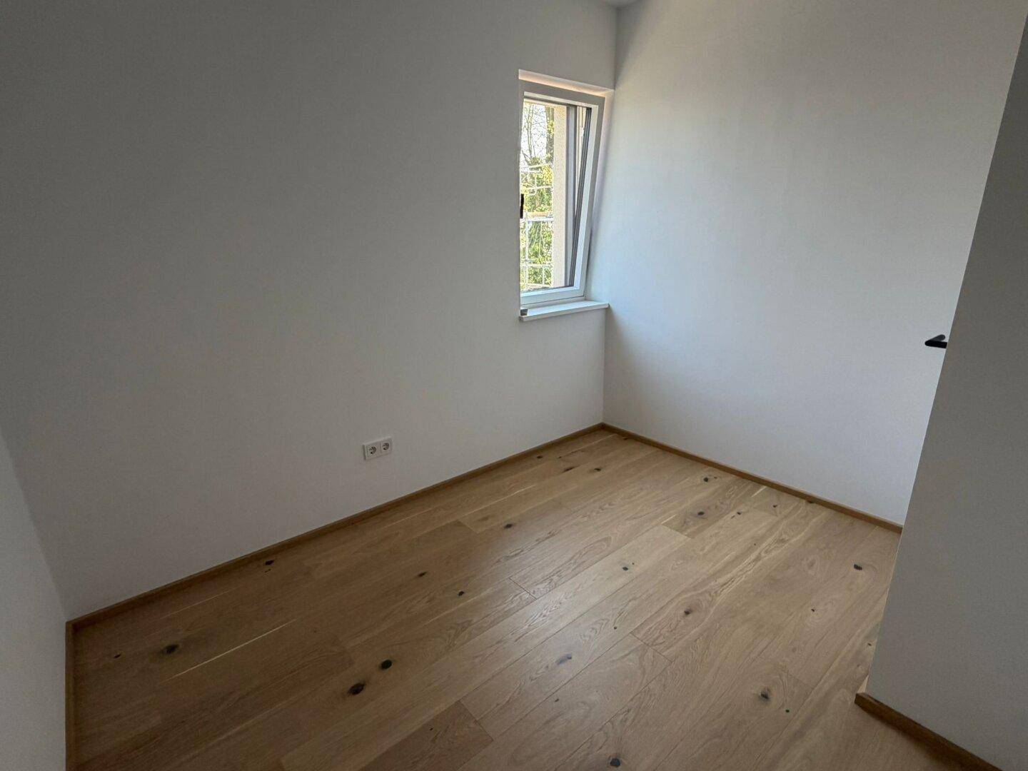 Kleineres Schlafzimmer oder Arbeitszimmer mit Eichenparkett und Fenster für natürliches Licht.
