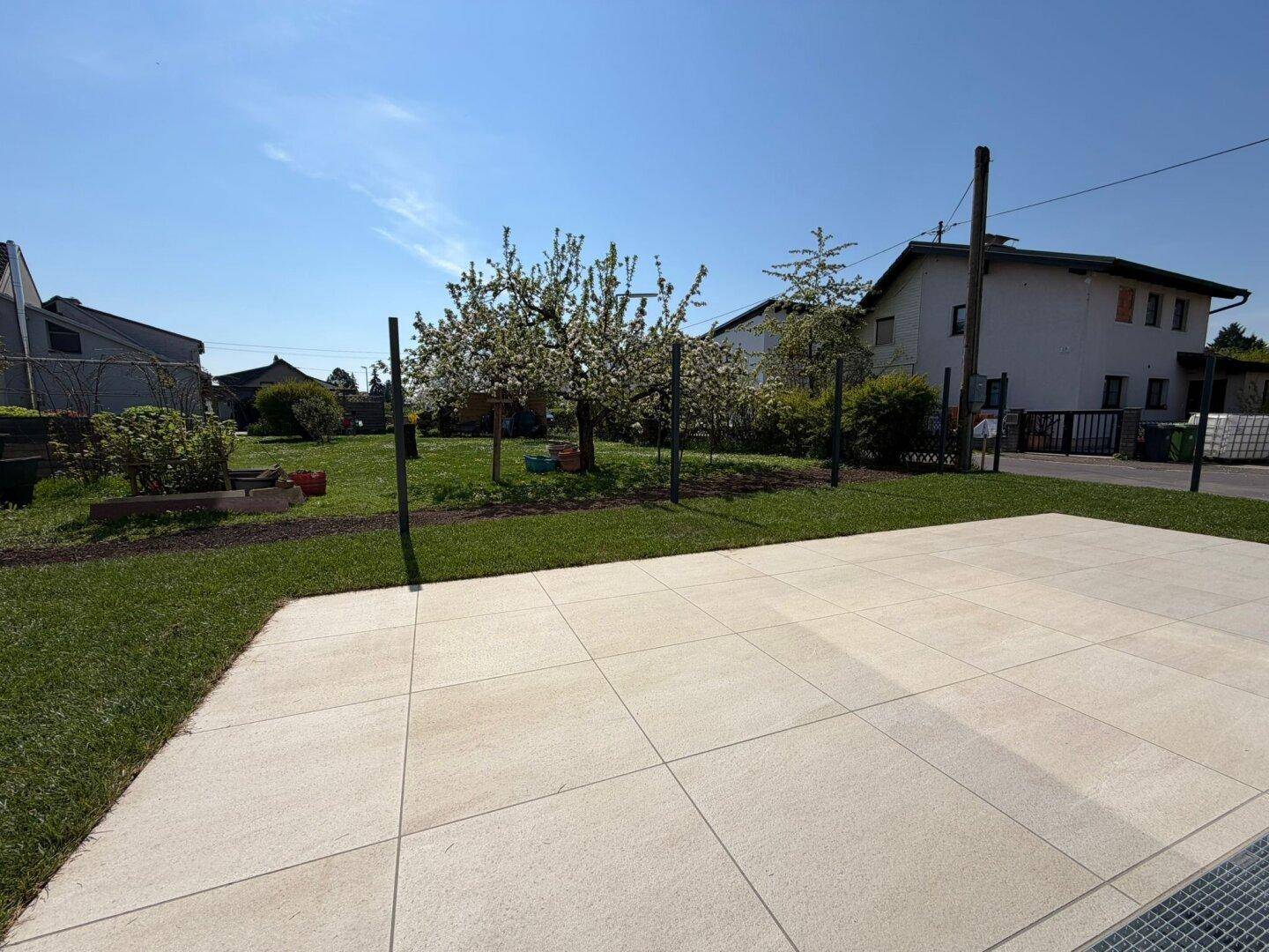 Helle Steinterrasse mit Blick auf den Garten und blühende Obstbäume im Hintergrund.
