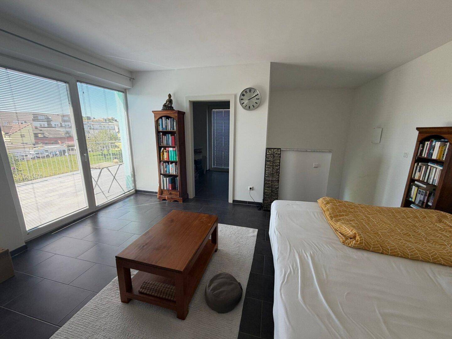 Geräumiges Schlafzimmer mit dunklen Fliesen, Bücherregalen und Zugang zum Balkon.