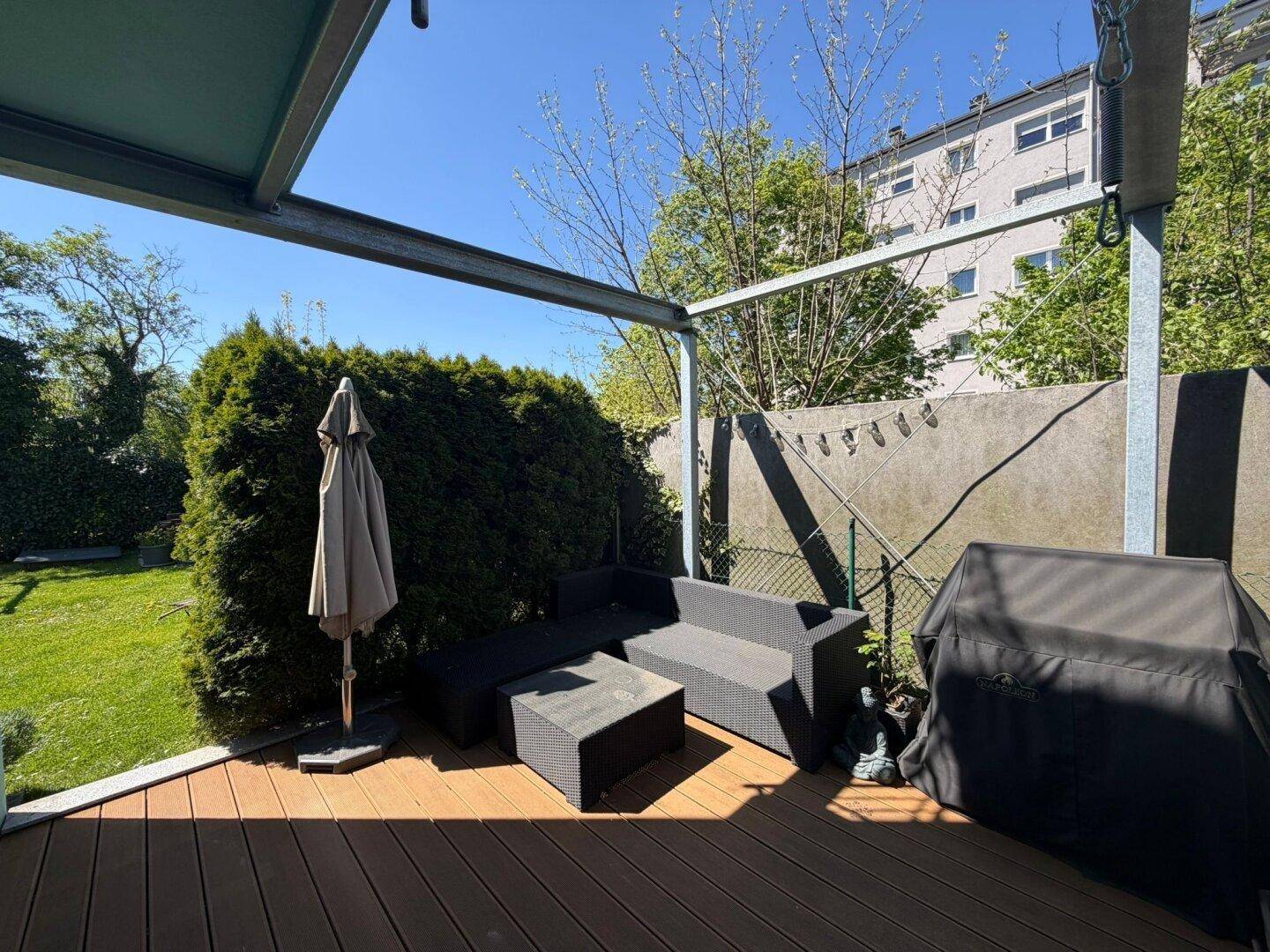 Möblierte Holzterrasse mit Grillbereich und Blick auf den gepflegten Garten.
