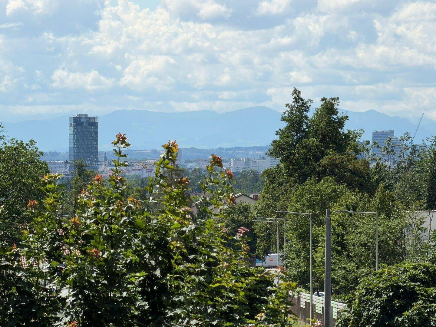 Weiter Blick über die Stadtlandschaft mit Bergen im Hintergrund an einem sonnigen Tag.
