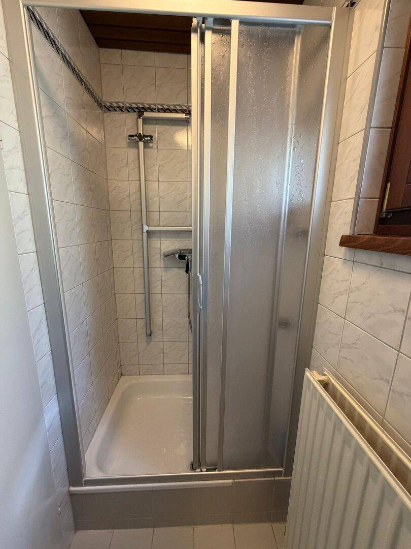 Duschbereich im Badezimmer mit weißen Fliesen und Duschkabine.