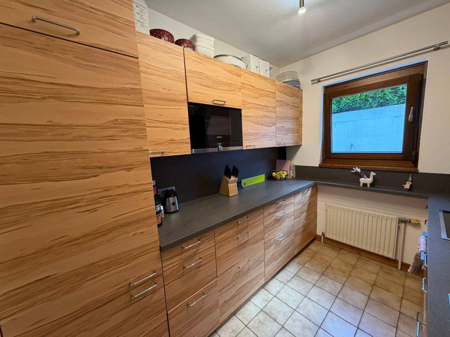 Helle Küche mit Holzschränken, dunkler Arbeitsplatte und integrierten Geräten.