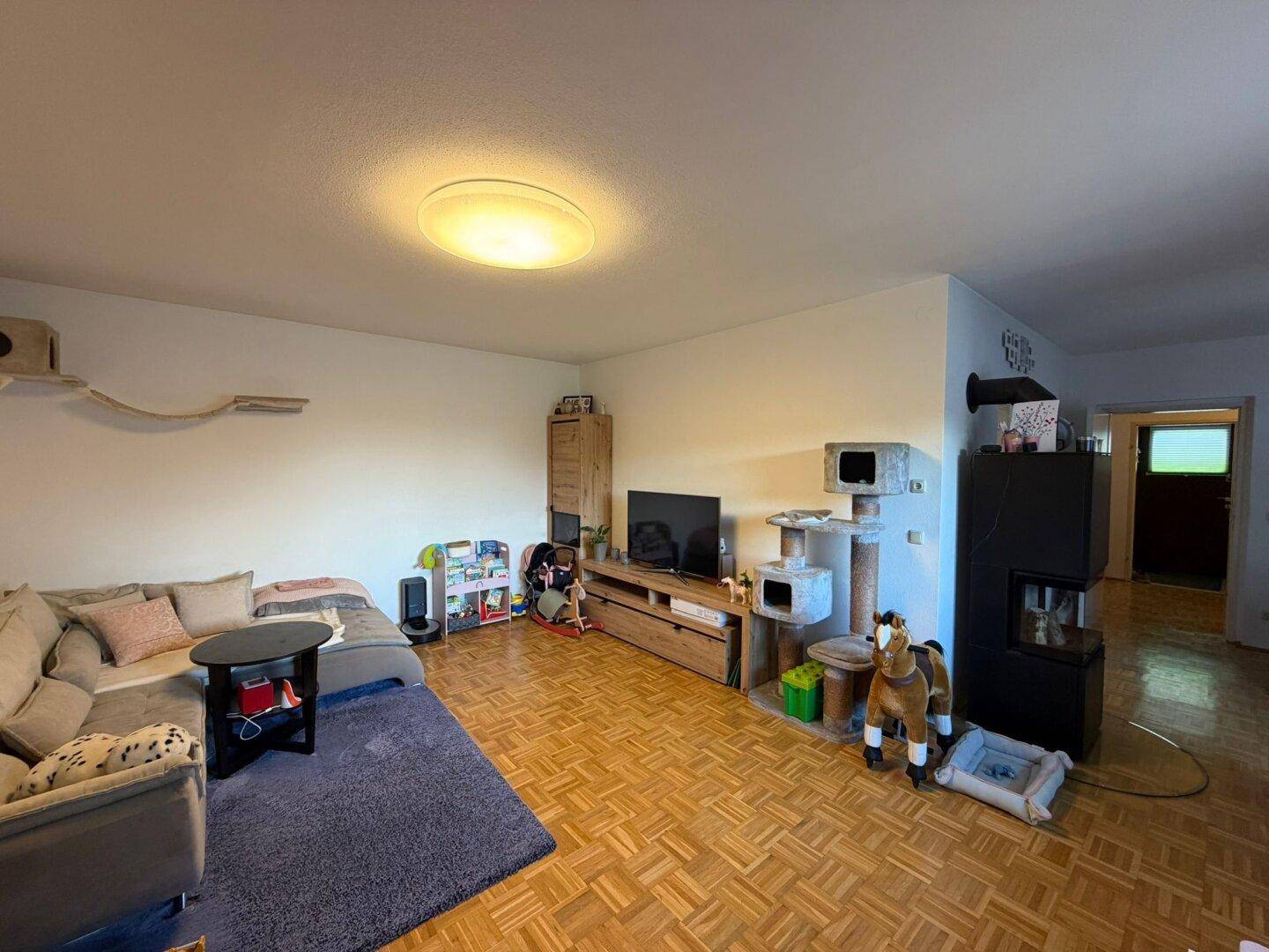 Gemütliches Wohnzimmer mit Parkettboden, Sofa, Kaminofen und Kinderspielzeug.