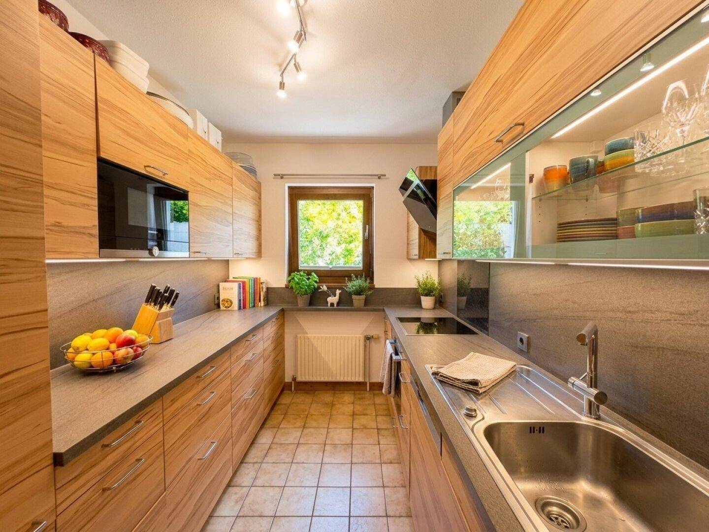 Moderne Küche mit Holzfronten, Einbaugeräten und Fenster mit Blick ins Grüne.