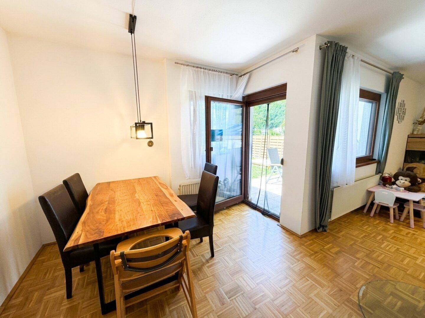 Essbereich mit Holztisch, Stühlen und Zugang zur Terrasse durch große Fenster.