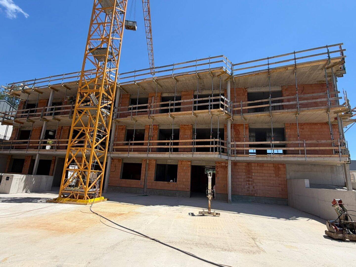 Baustelle eines neuen Gebäudes mit sichtbaren Ziegelwänden und Betonstrukturen im Baufortschritt.
