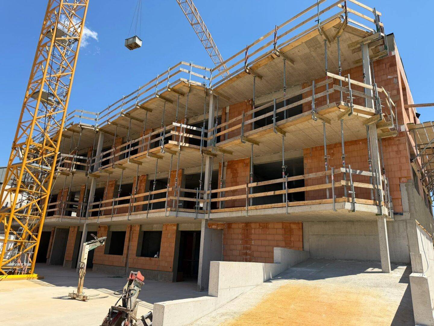 Fortschreitender Neubau mit mehreren Etagen und Baugerüst bei strahlendem Sonnenschein.