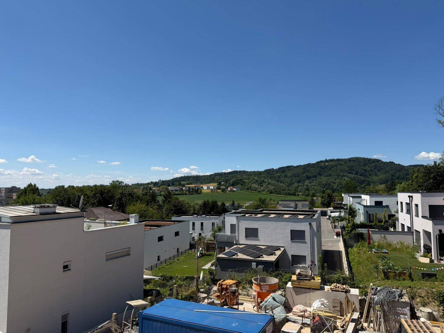 Panoramablick von einer Baustelle über moderne Wohngebäude mit Flachdächern und weiten grünen Feldern.