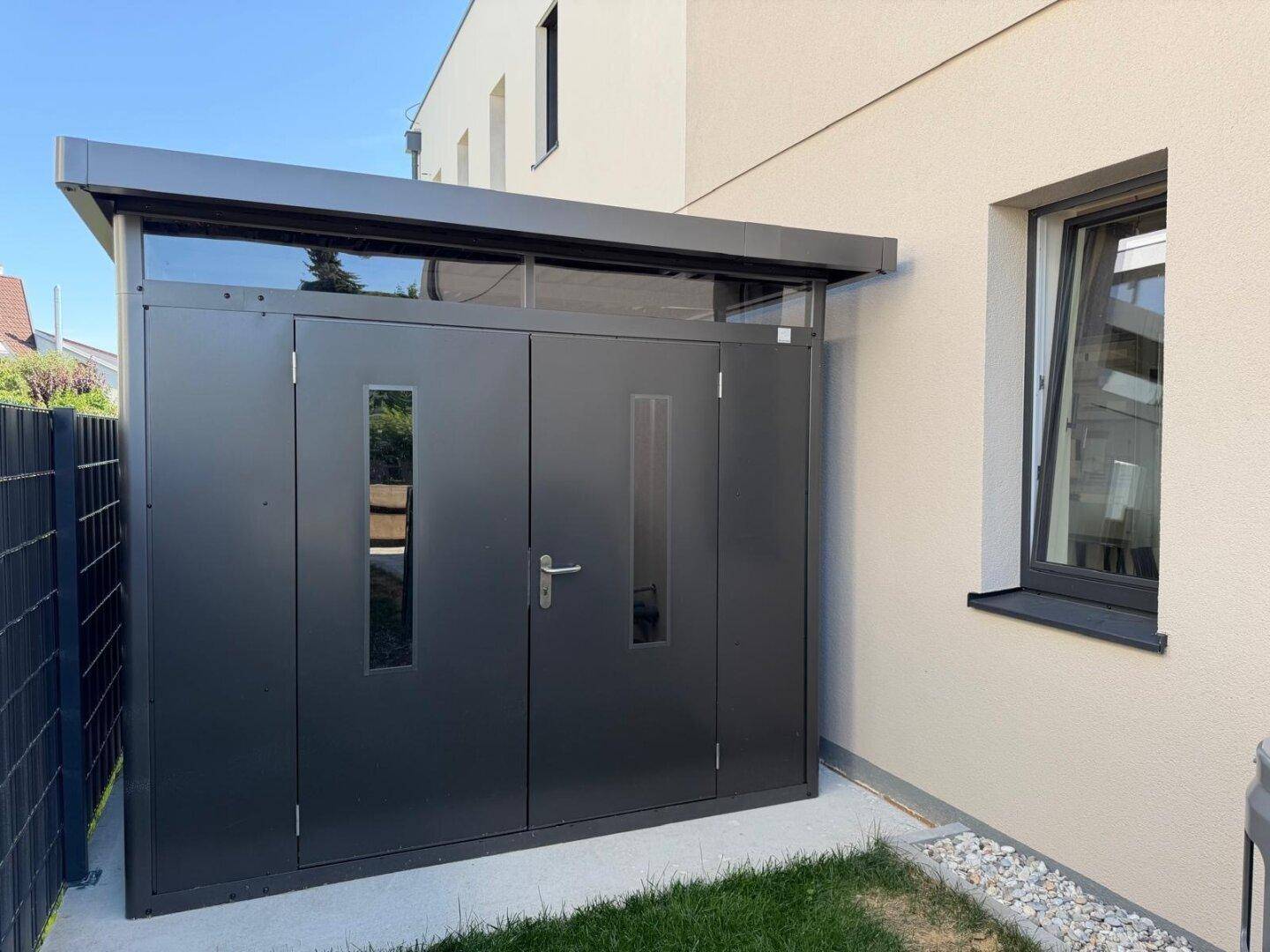 Moderner Geräteschuppen mit dunkler Fassade und Fenster neben dem Haus.