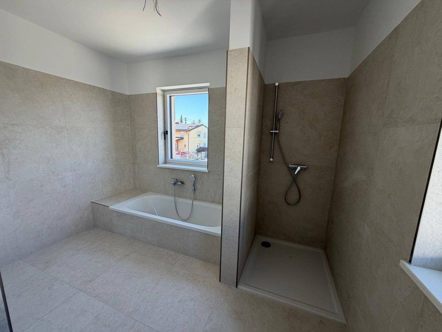 Helles Badezimmer mit Badewanne, ebenerdiger Dusche und Fenster.