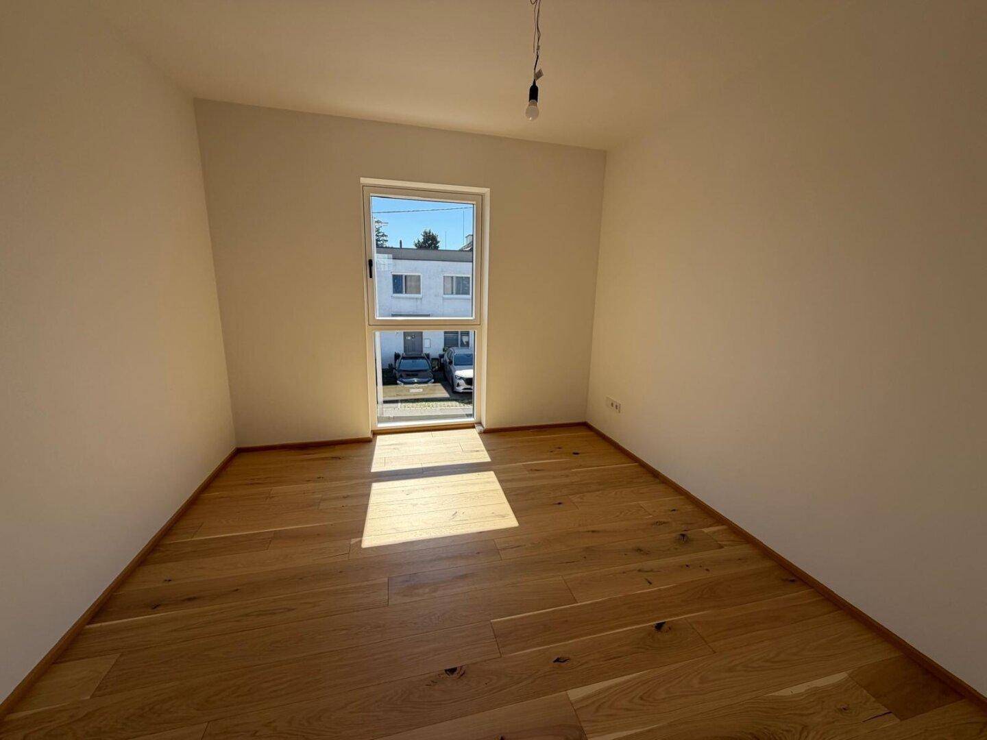 Freundliches Zimmer mit Parkettboden und Ausblick auf die Umgebung.