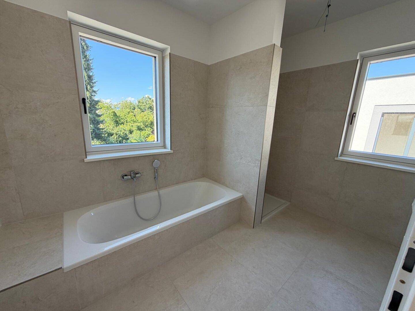 Modernes Badezimmer mit Badewanne, Duschbereich und zwei Fenstern.