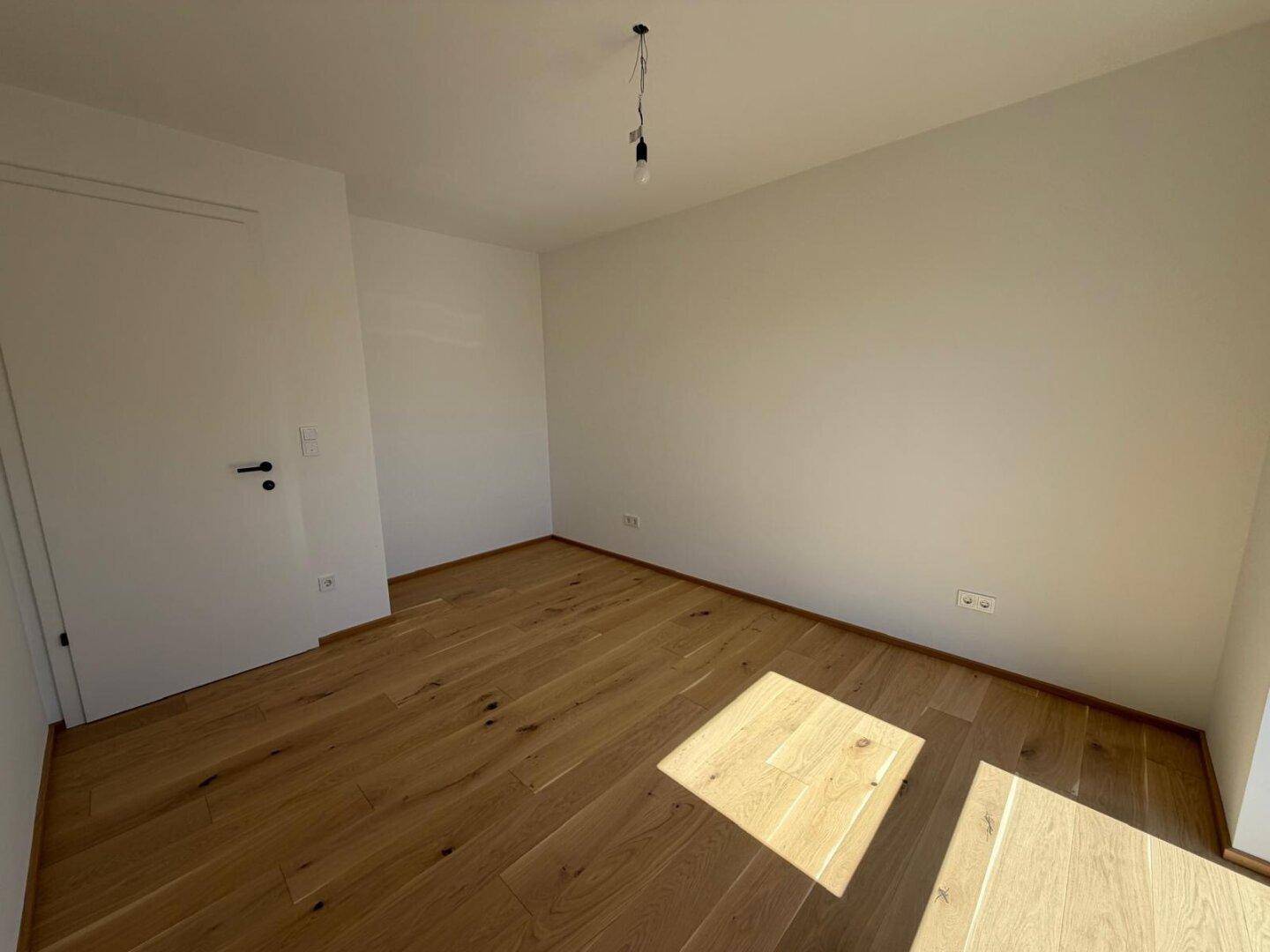 Ruhiges Schlafzimmer mit hellem Parkettboden und viel Tageslicht.