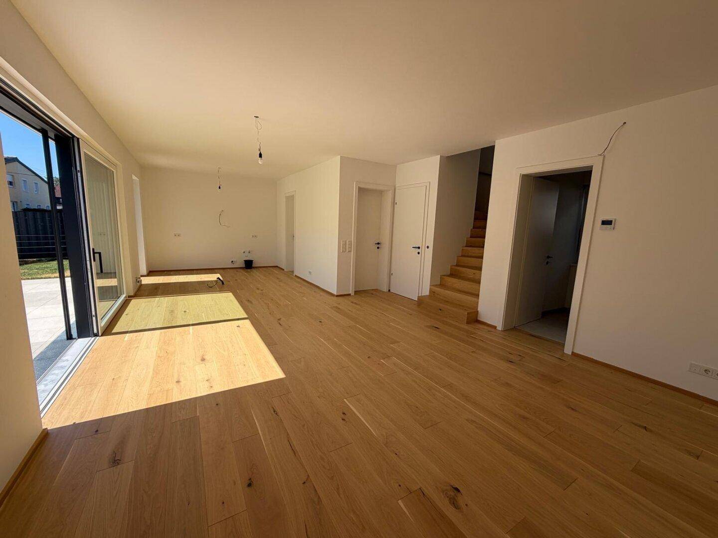Heller, leerer Wohnbereich mit Eichenparkettboden und Zugang zur Terrasse.