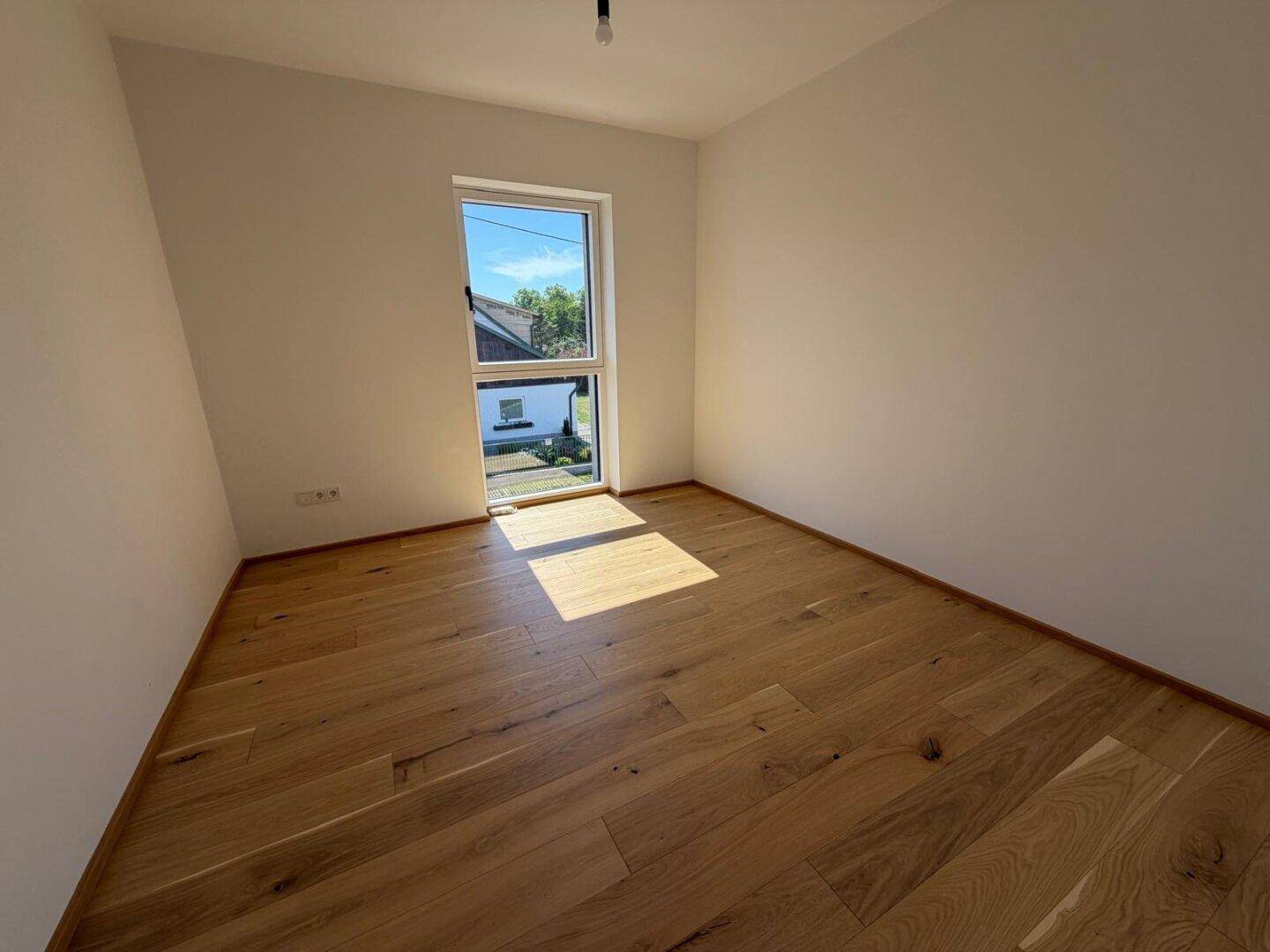 Helles Zimmer mit Eichenparkett und Fenster mit Blick ins Grüne.