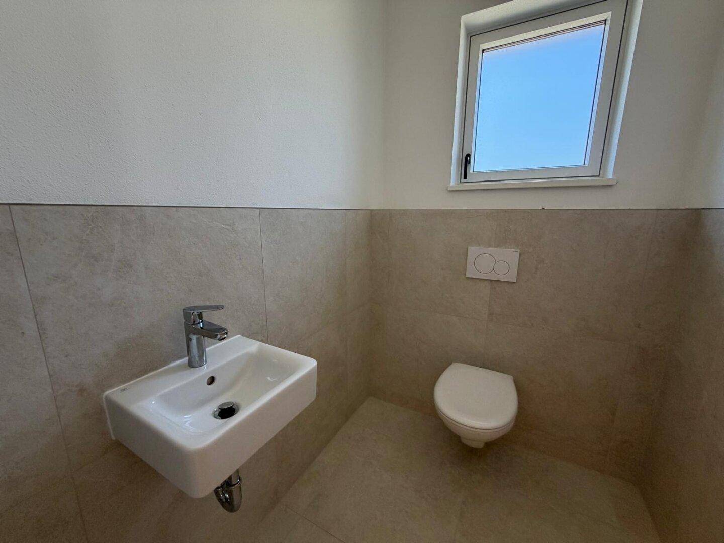 Separates Gäste-WC mit wandhängendem WC, Waschbecken und Fenster.
