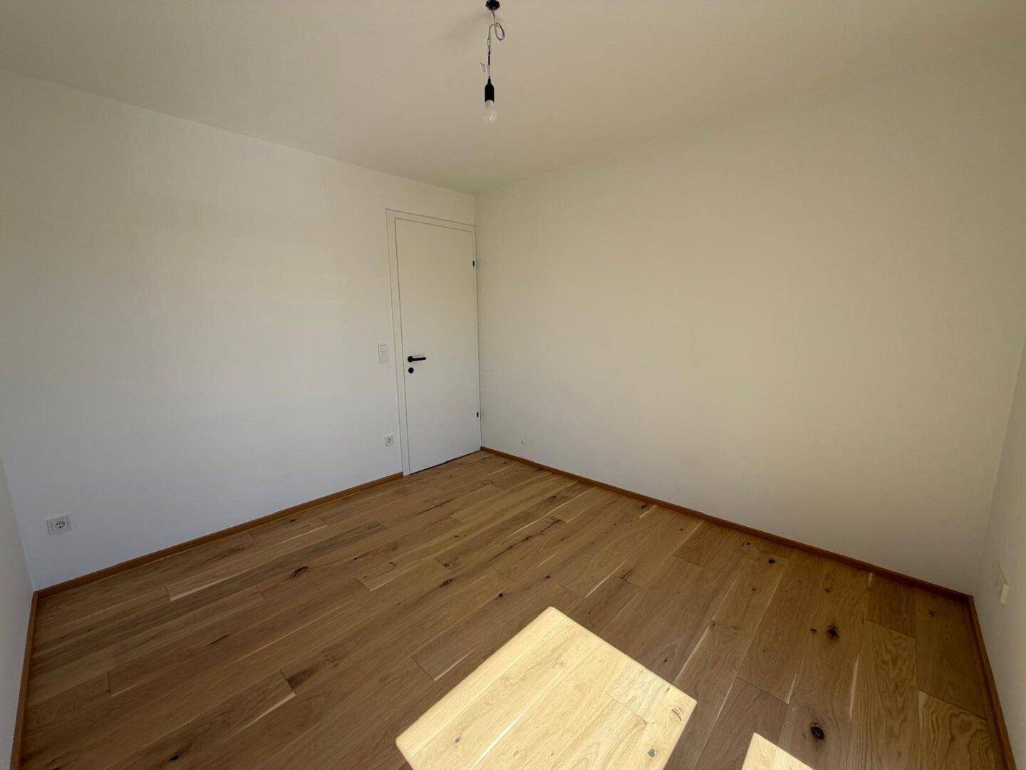 Geräumiges Schlafzimmer mit hellem Parkettboden und weiß gestrichenen Wänden.