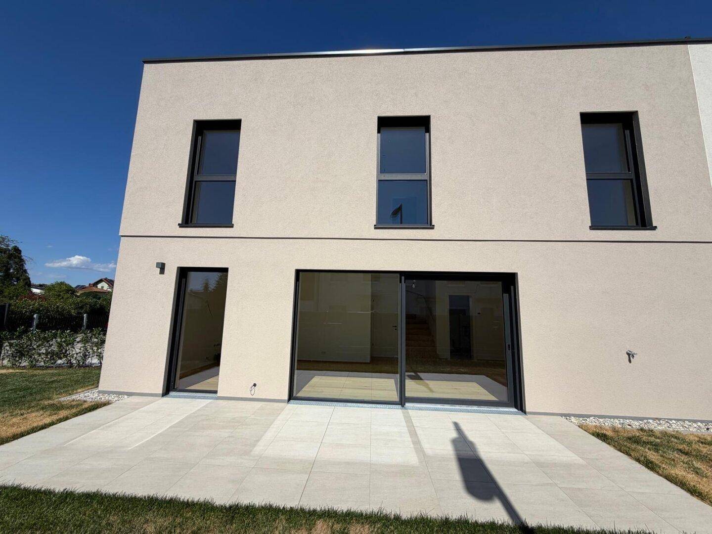 Rückseite des Neubaus mit großer, heller Terrasse und bodentiefen Fenstern.