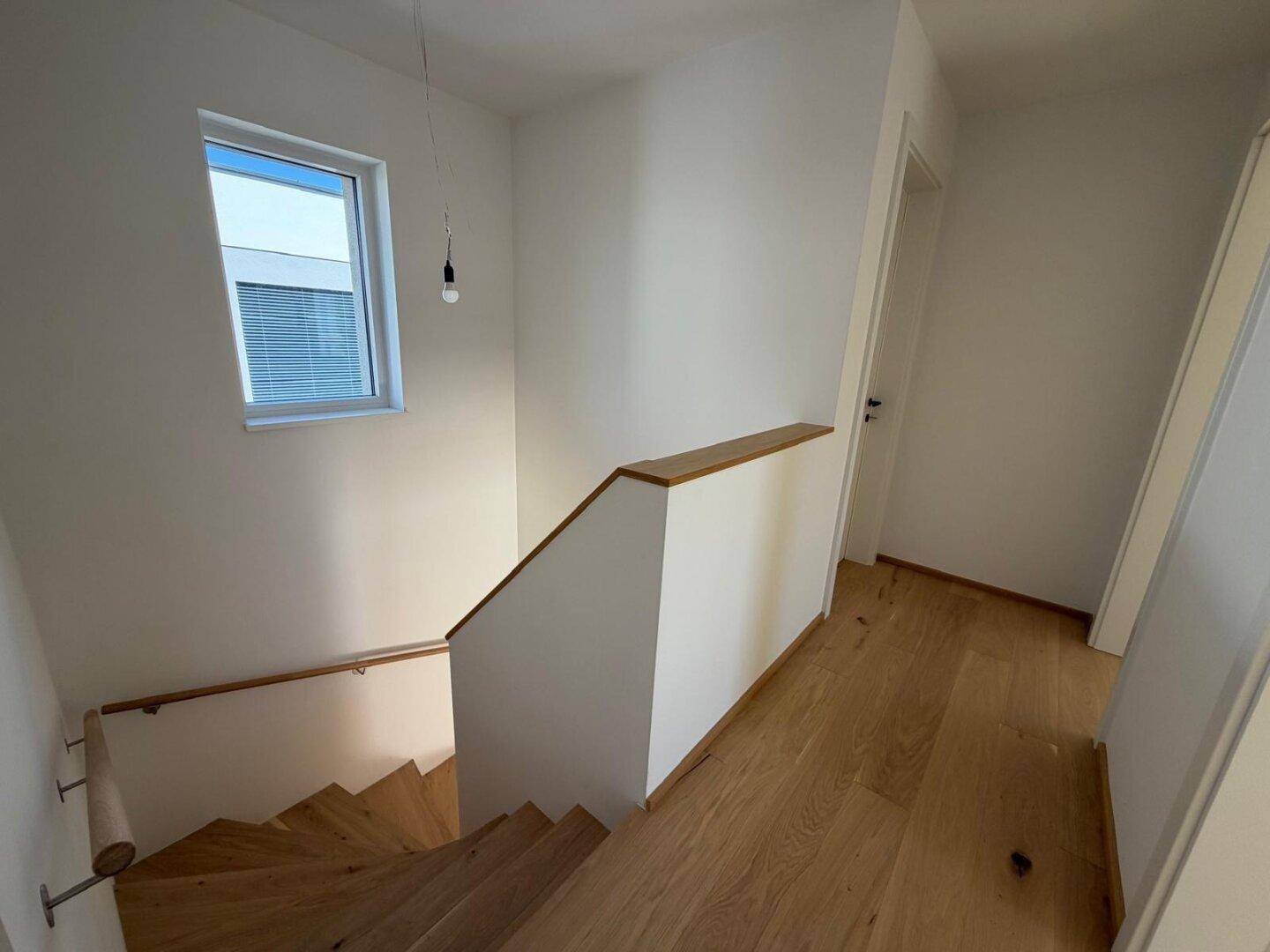 Heller Flur mit Holztreppe und Fenster, das Tageslicht hereinlässt.