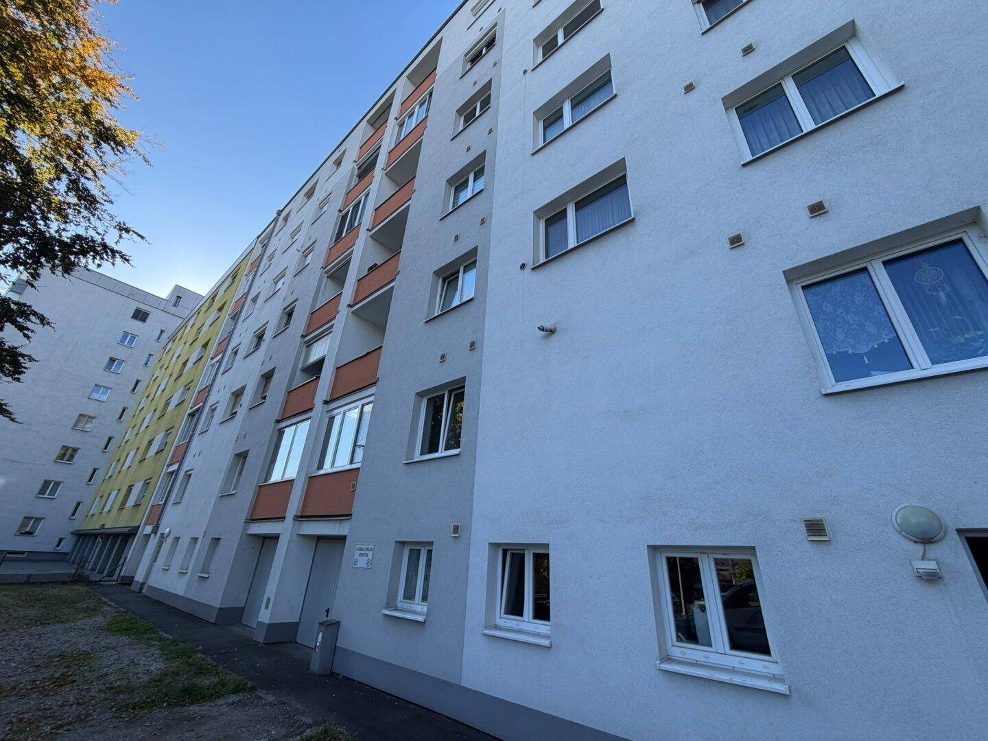 Fassade eines Mehrfamilienhauses mit vielen Fenstern und Balkonen unter klarem Himmel.