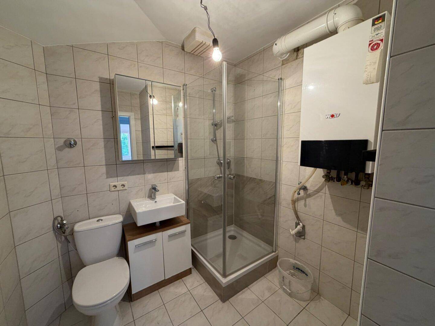 Funktionales Badezimmer mit beigen Fliesen, Duschkabine, WC und Waschbecken mit Spiegelschrank.