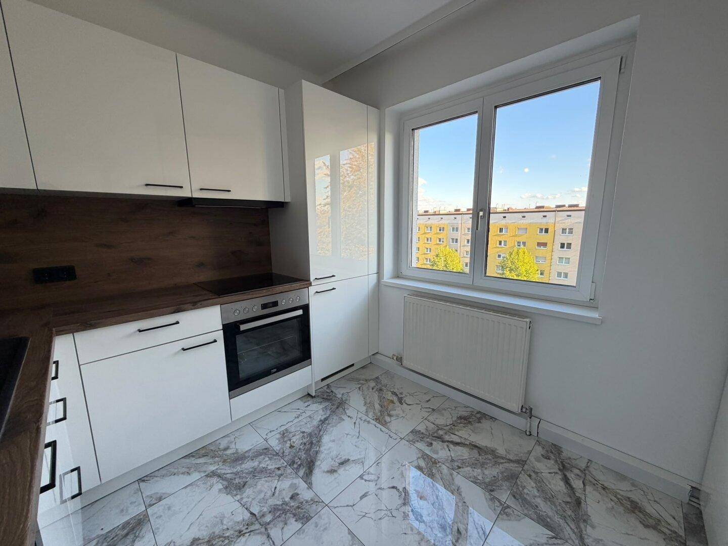 Helle, moderne Küche mit weißen Schränken, Holzoptik-Arbeitsplatten und großem Fenster.