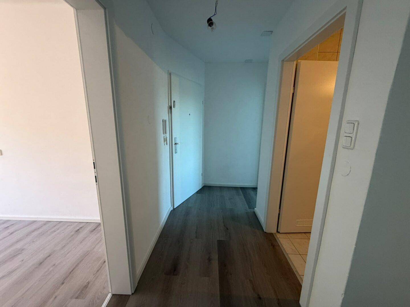 Heller Flur mit dunklem Laminatboden und weißen Wänden, der zu verschiedenen Räumen führt.