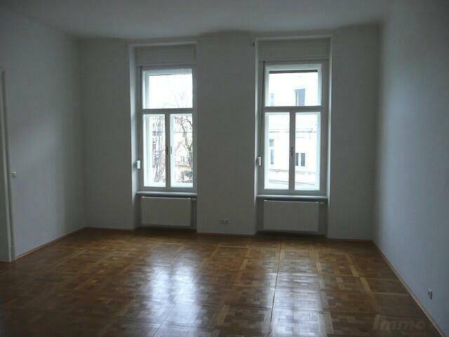 Geräumiges Wohnzimmer mit klassischem Parkettboden und viel Tageslicht durch zwei Fenster.