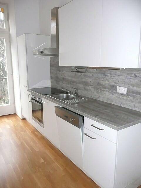 Moderne Einbauküche mit weißen Schränken, Holzoptik-Arbeitsplatte und Zugang zum Balkon.