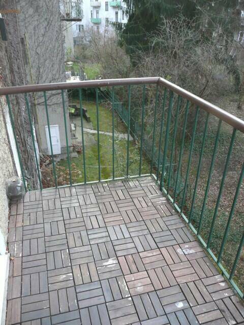 Kleiner Balkon mit Holzdielen und Blick auf den grünen Innenhof und Gartenbereich.