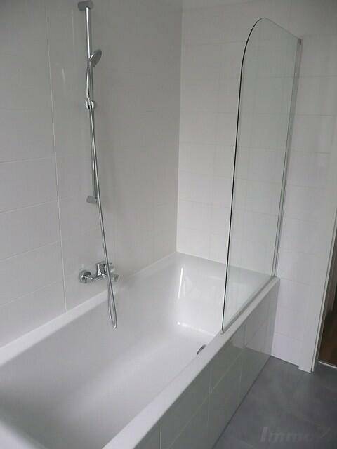 Badewanne mit Duschfunktion und Glasabtrennung in einem hell gefliesten Badezimmer.