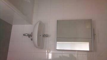 Badezimmer mit weiß gefliesten Wänden, Waschbecken und Spiegelschrank.