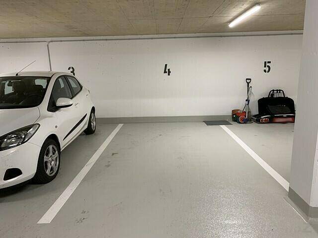 Ein sauberer Tiefgaragenstellplatz mit einem weißen Kleinwagen und Lagerbereich im Hintergrund.