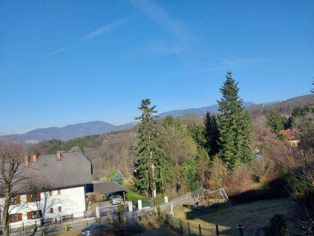 Weitläufiger Blick auf die umliegende Landschaft mit Bergen, Wald und einem Spielplatz im Vordergrund.