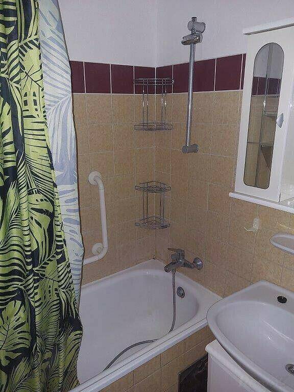 Badezimmer mit Badewanne, Duschvorhang und Handlauf, gefliest in Beige und Bordeaux.