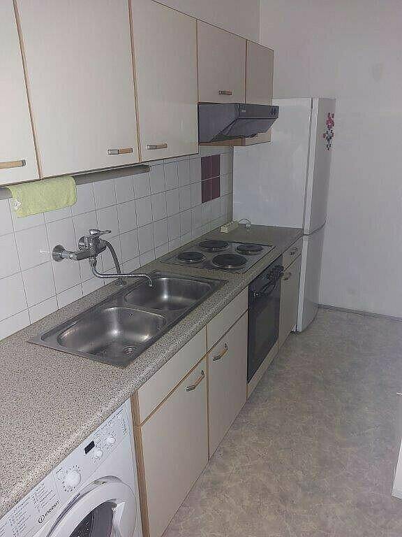 Kleine Küche mit Einbauschränken, Spüle, Herd und Kühlschrank in hellem Design.