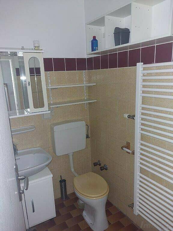 WC-Bereich mit Toilette, Waschbecken und Handtuchheizkörper, gefliest in Beige und Bordeaux.