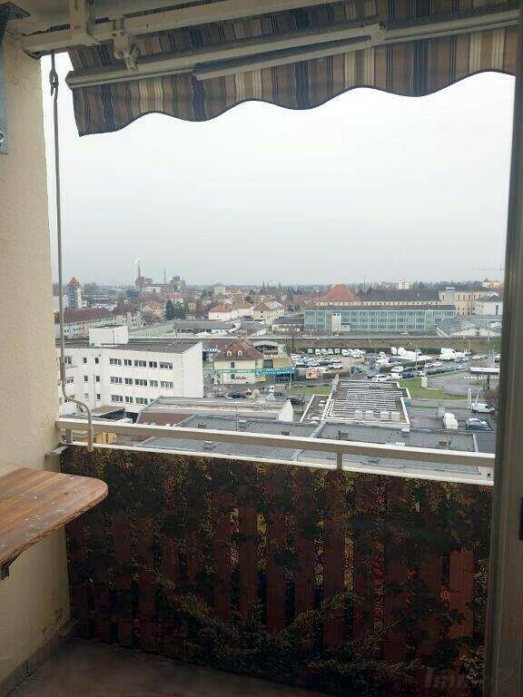 Blick von einem Balkon auf die städtische Umgebung mit Gebäuden und einem Parkplatz.
