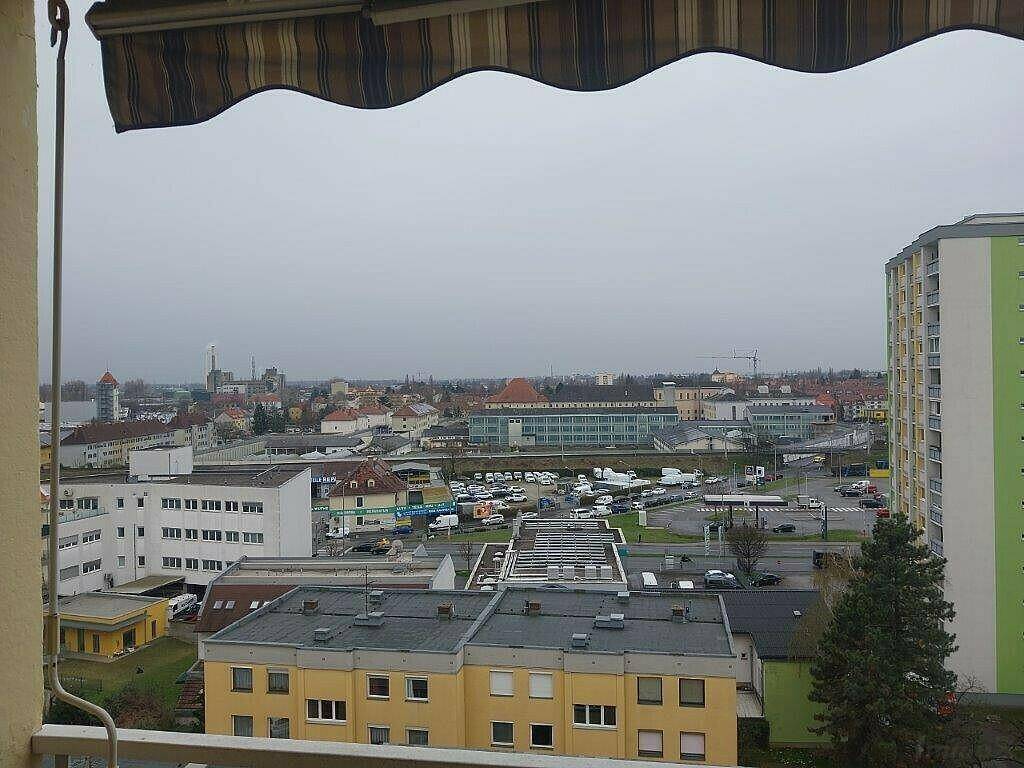 Weitläufiger Blick über die Stadt mit Gebäuden und einem Parkplatz unter bewölktem Himmel.