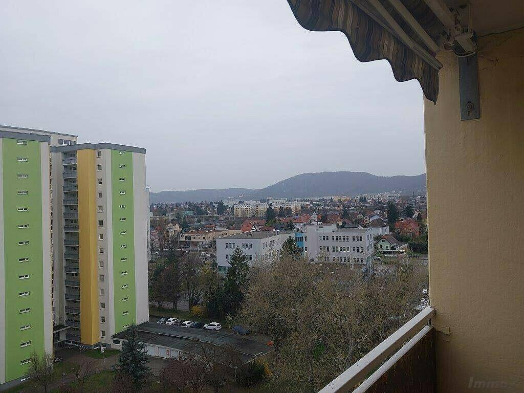 Panoramablick über die Stadt mit hohen Gebäuden und bewaldeten Hügeln im Hintergrund.