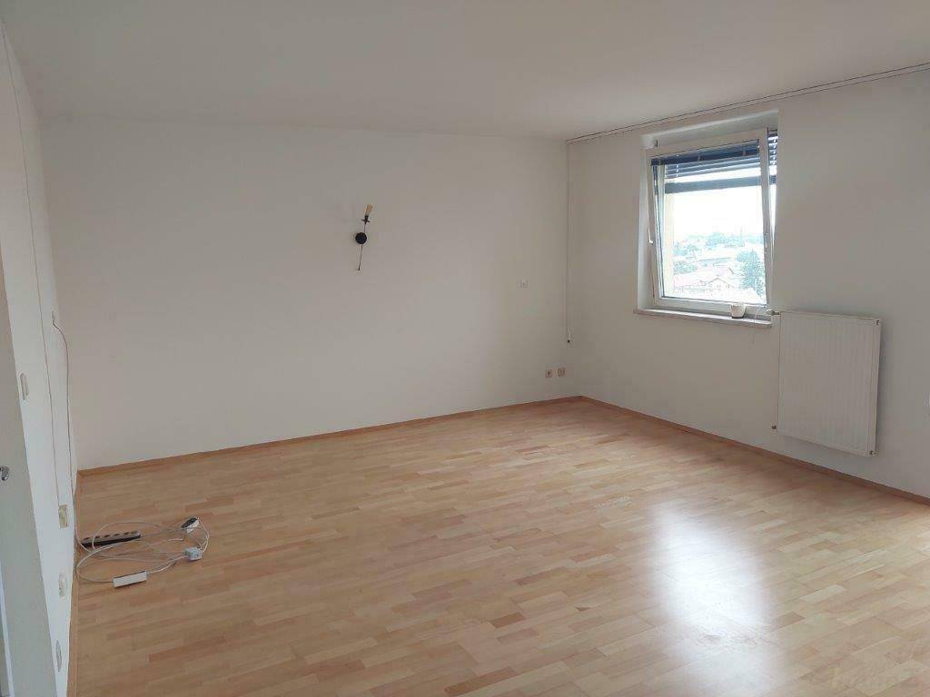 Geräumiger, heller Wohnraum mit Laminatboden und einem Fenster mit Blick nach draußen.