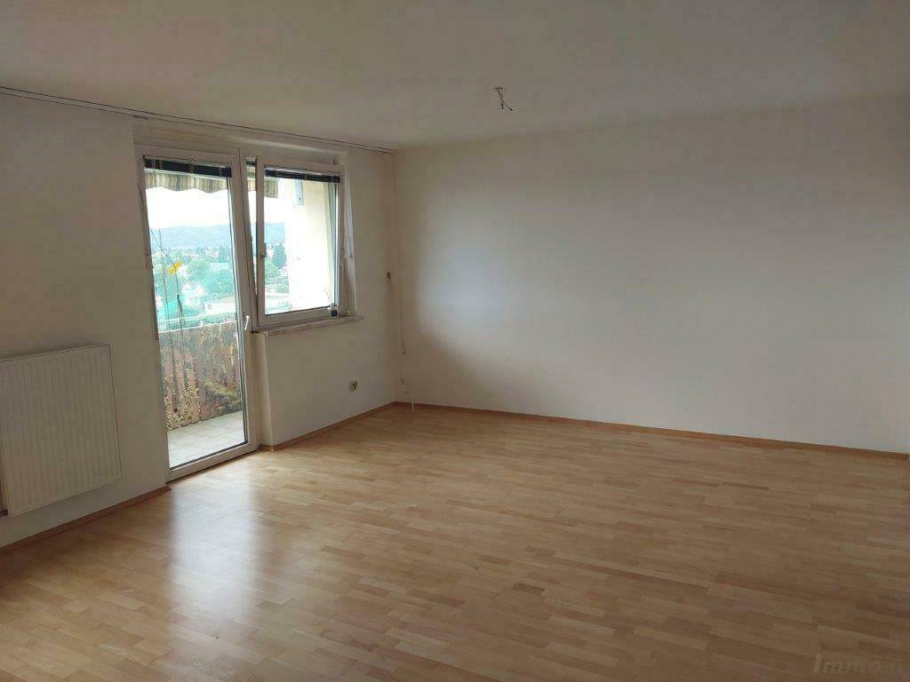 Heller Wohnraum mit hellem Laminatboden und Zugang zu einem Balkon.