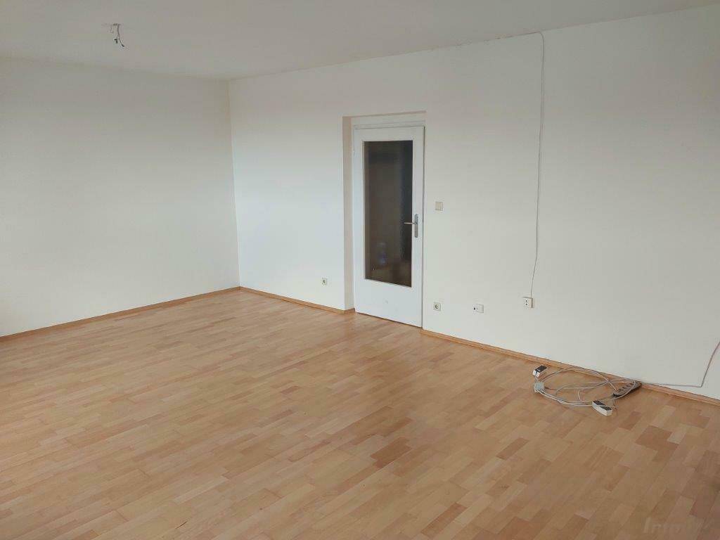 Heller Wohnraum mit Laminatboden und einer Tür, die zu einem anderen Bereich führt.