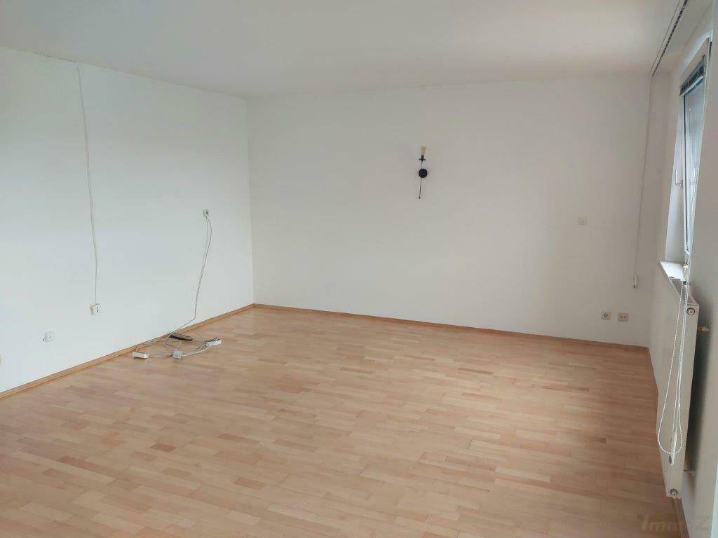 Leerer Wohnraum mit hellem Laminatboden und weißen Wänden, bereit zur Einrichtung.
