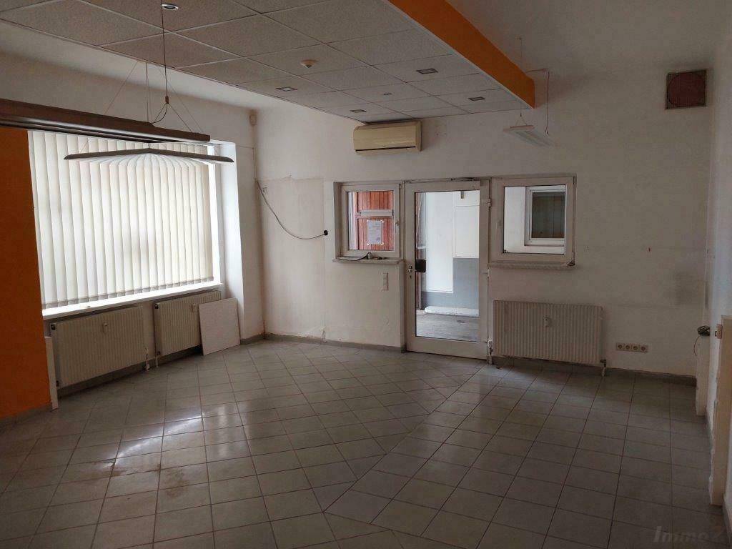 Geräumiger Büroraum mit Fliesenboden, großen Fenstern und abgehängter Decke.
