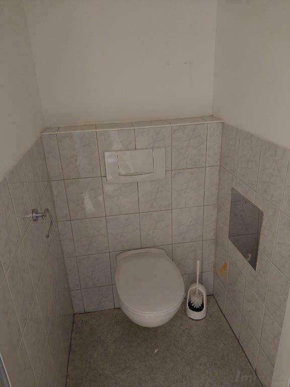 Einfache Gästetoilette mit gefliesten Wänden, wandhängendem WC und Spülkasten.