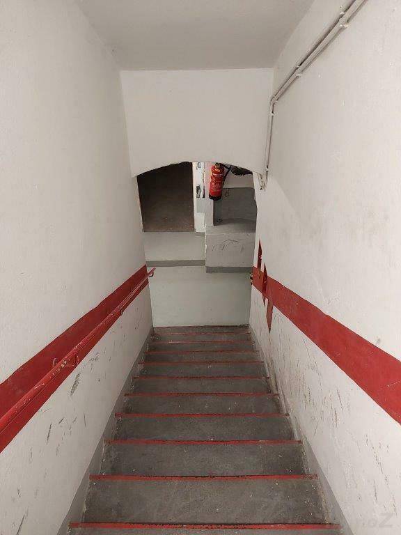 Kellertreppe mit roten Handläufen und einem Feuerlöscher im Hintergrund.