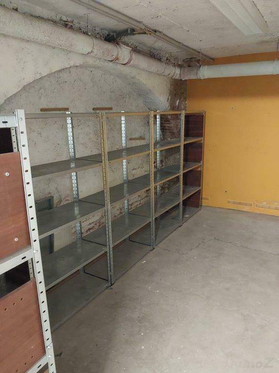 Kellerraum mit gewölbter Decke, Betonboden und Metallregalen an der Wand.